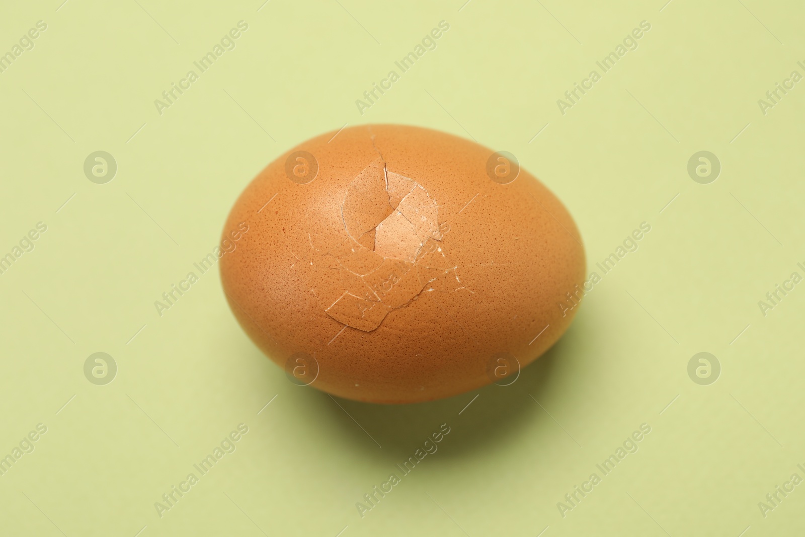 Photo of One egg with cracked shell on light green background, above view