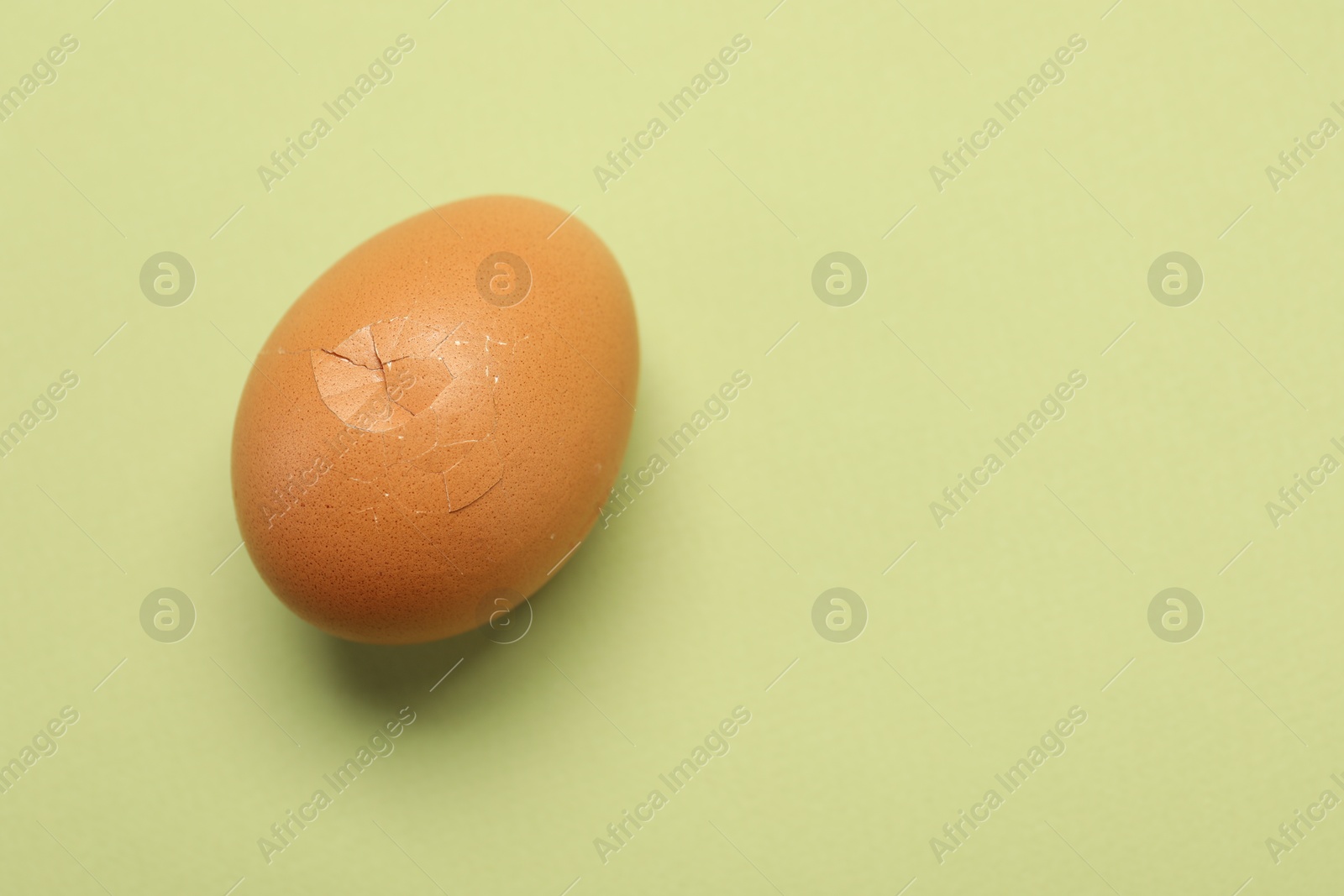 Photo of One egg with cracked shell on light green background, closeup. Space for text