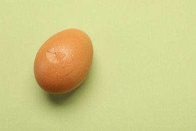 One egg with cracked shell on light green background, closeup. Space for text