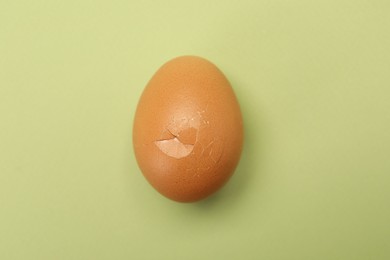 Photo of One egg with cracked shell on light green background, top view