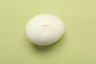 Photo of One egg with cracked shell on light green background, top view