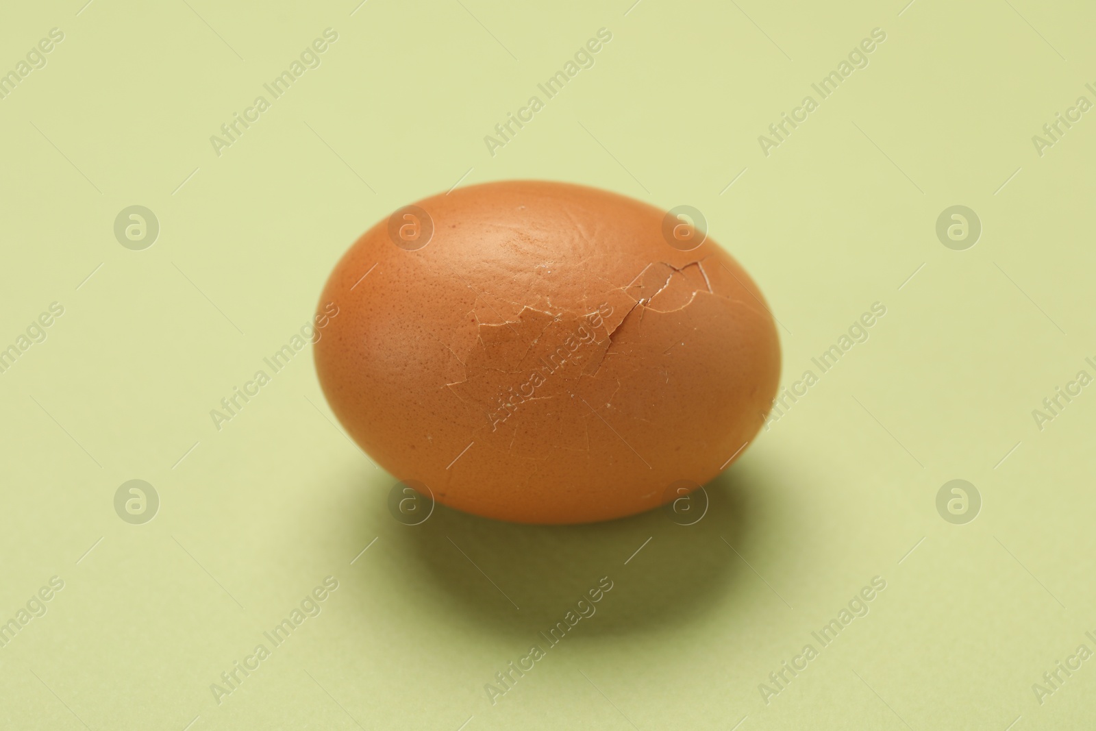 Photo of One egg with cracked shell on light green background, closeup