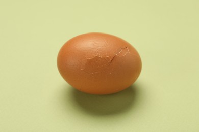 Photo of One egg with cracked shell on light green background, closeup