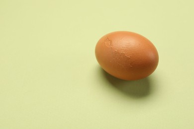 Photo of One egg with cracked shell on light green background. Space for text