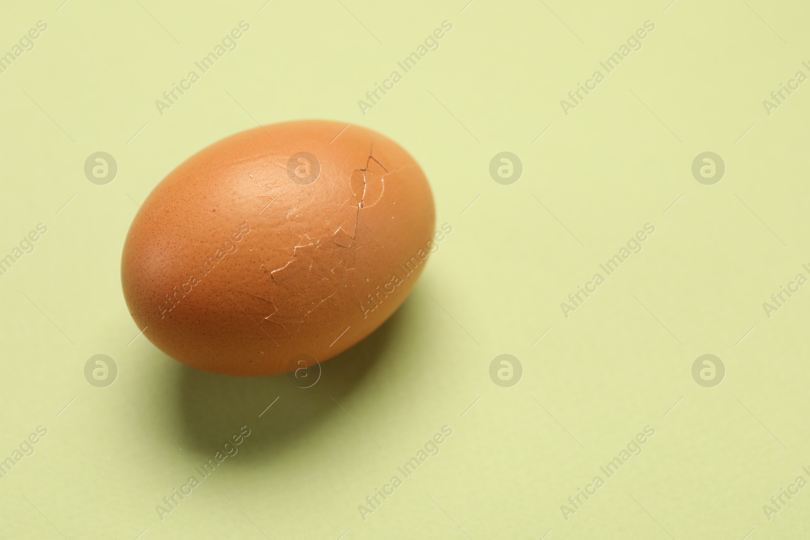 Photo of One egg with cracked shell on light green background, closeup. Space for text