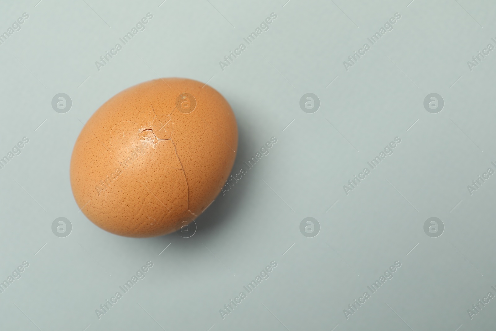 Photo of One egg with cracked shell on grey background, top view. Space for text