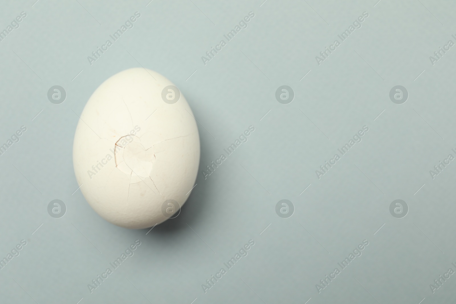 Photo of One egg with cracked shell on grey background, top view. Space for text