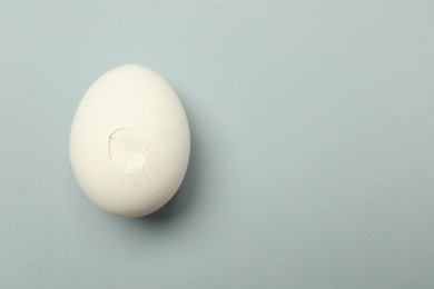 One egg with cracked shell on grey background, top view. Space for text