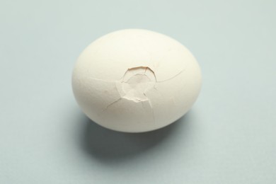 Photo of One egg with cracked shell on grey background, closeup