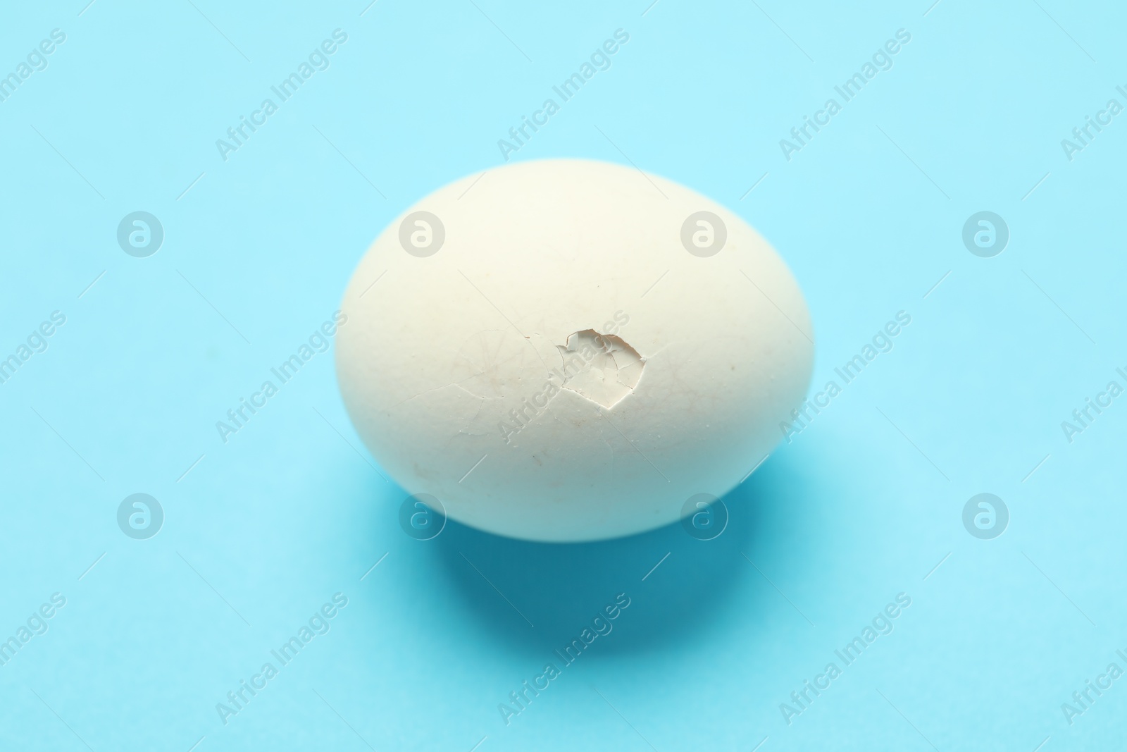 Photo of One egg with cracked shell on light blue background