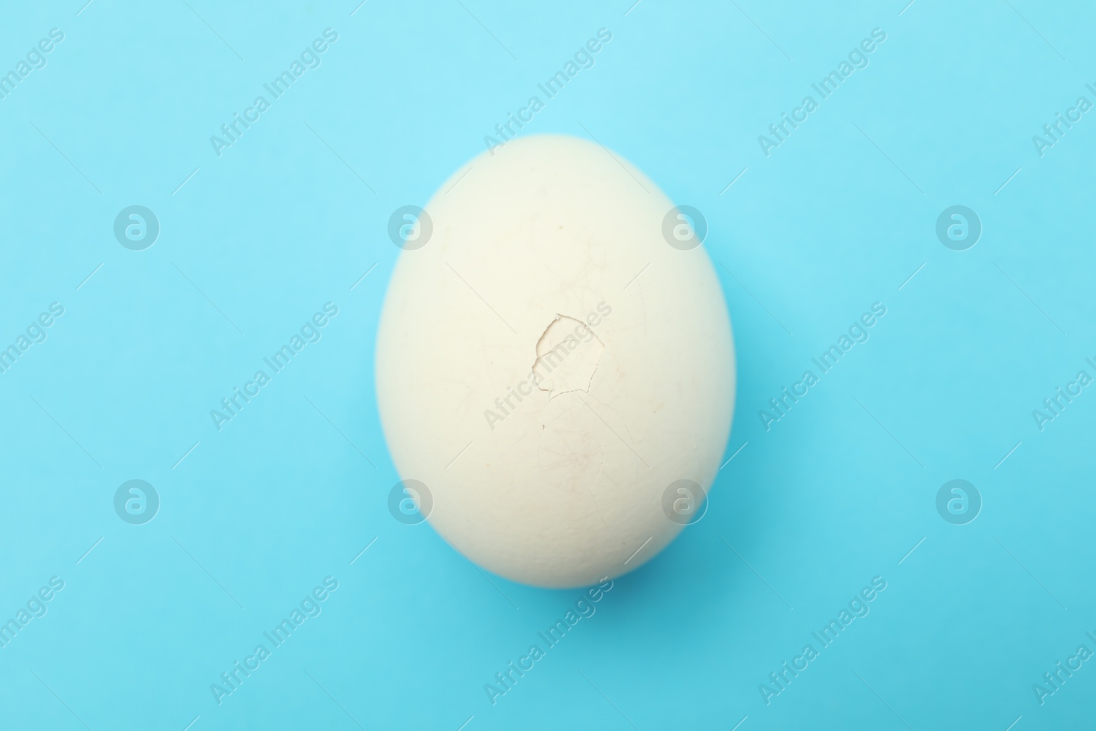 Photo of One egg with cracked shell on light blue background, top view