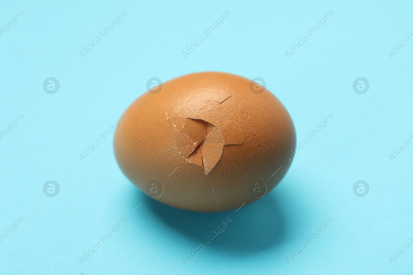 Photo of One egg with cracked shell on light blue background, closeup