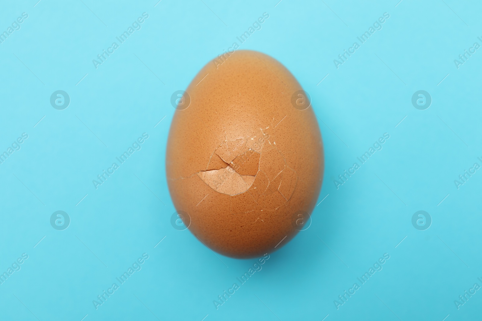 Photo of One egg with cracked shell on light blue background, top view