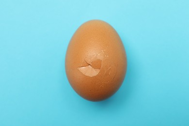 One egg with cracked shell on light blue background, top view