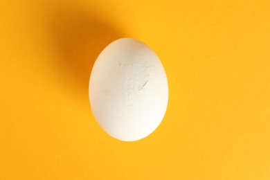 One egg with cracked shell on orange background, top view