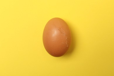 One egg with cracked shell on yellow background, top view