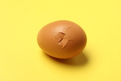 Photo of One egg with cracked shell on yellow background, closeup