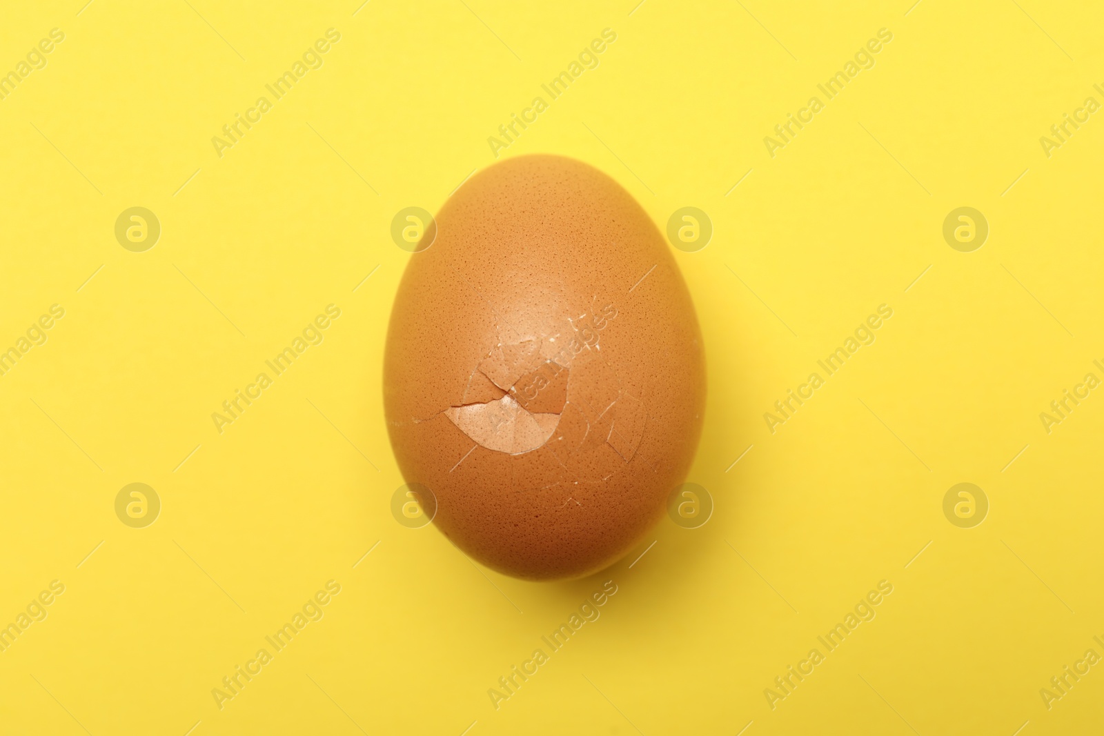 Photo of One egg with cracked shell on yellow background, top view