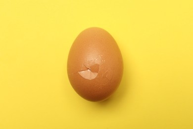 Photo of One egg with cracked shell on yellow background, top view