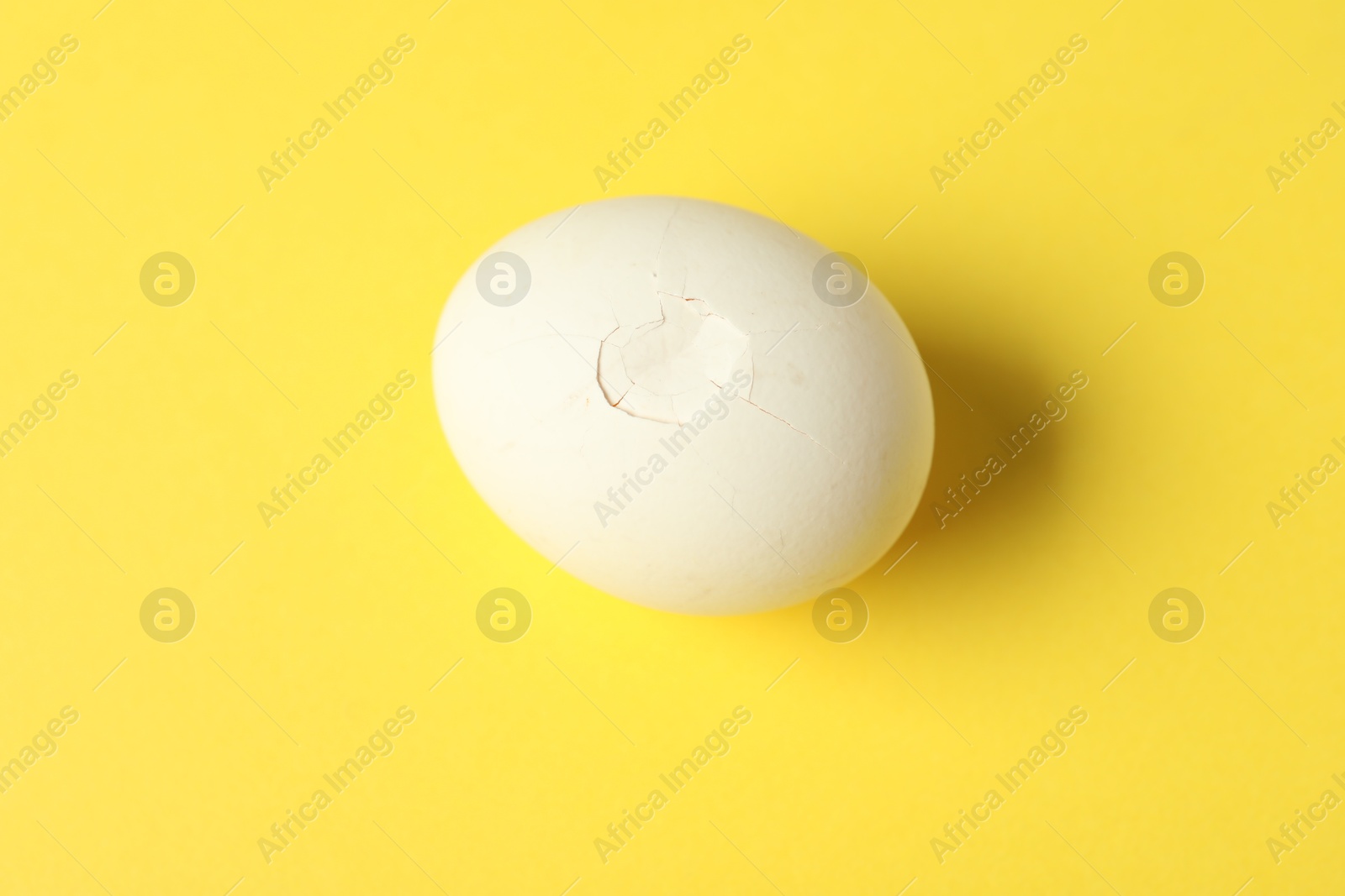 Photo of One egg with cracked shell on yellow background, top view