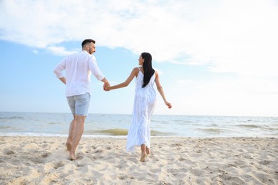 Photo of Happy couple running together on beach, back view