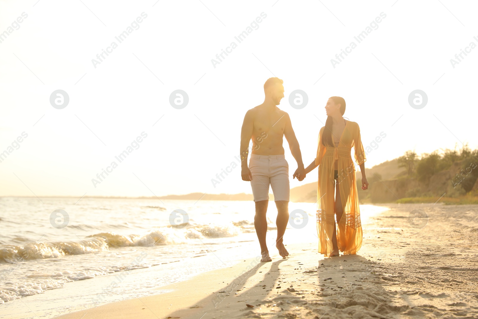 Photo of Happy young couple walking together on beach at sunset