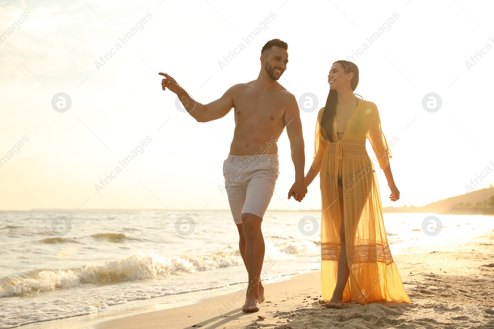 Photo of Happy young couple walking together on beach at sunset