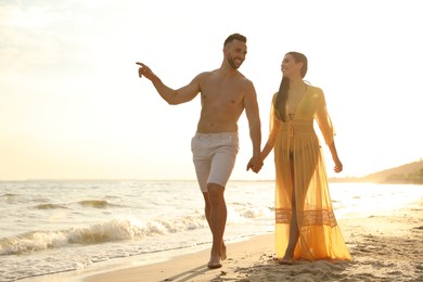 Photo of Happy young couple walking together on beach at sunset