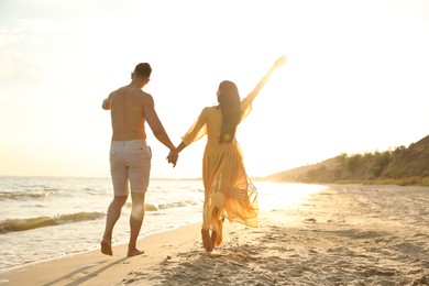 Photo of Lovely couple walking together on beach at sunset, back view