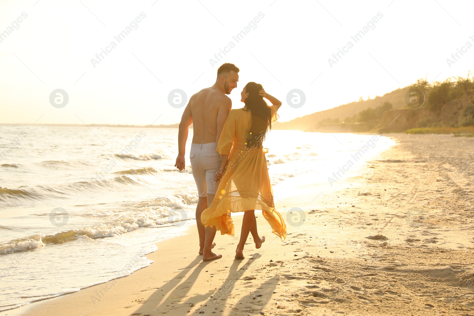 Photo of Happy couple walking together on beach at sunset, back view