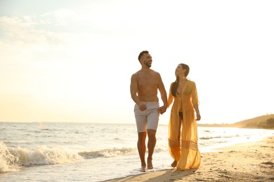 Photo of Happy young couple walking together on beach at sunset