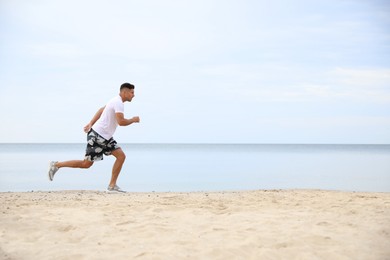 Photo of Muscular man running on beach, space for text. Body training