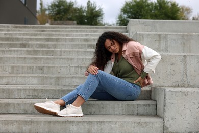 Photo of Woman with injured back on stairs outdoors after fall. Dangerous accident