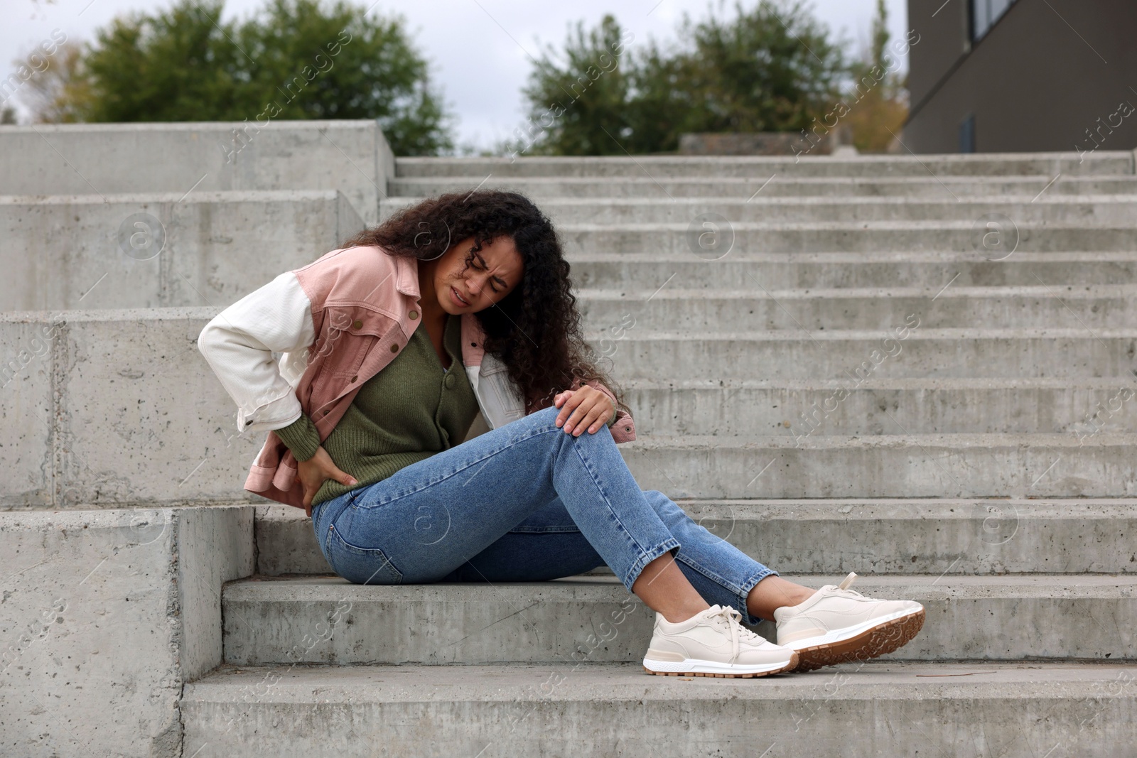 Photo of Woman with injured back on stairs outdoors after fall. Dangerous accident