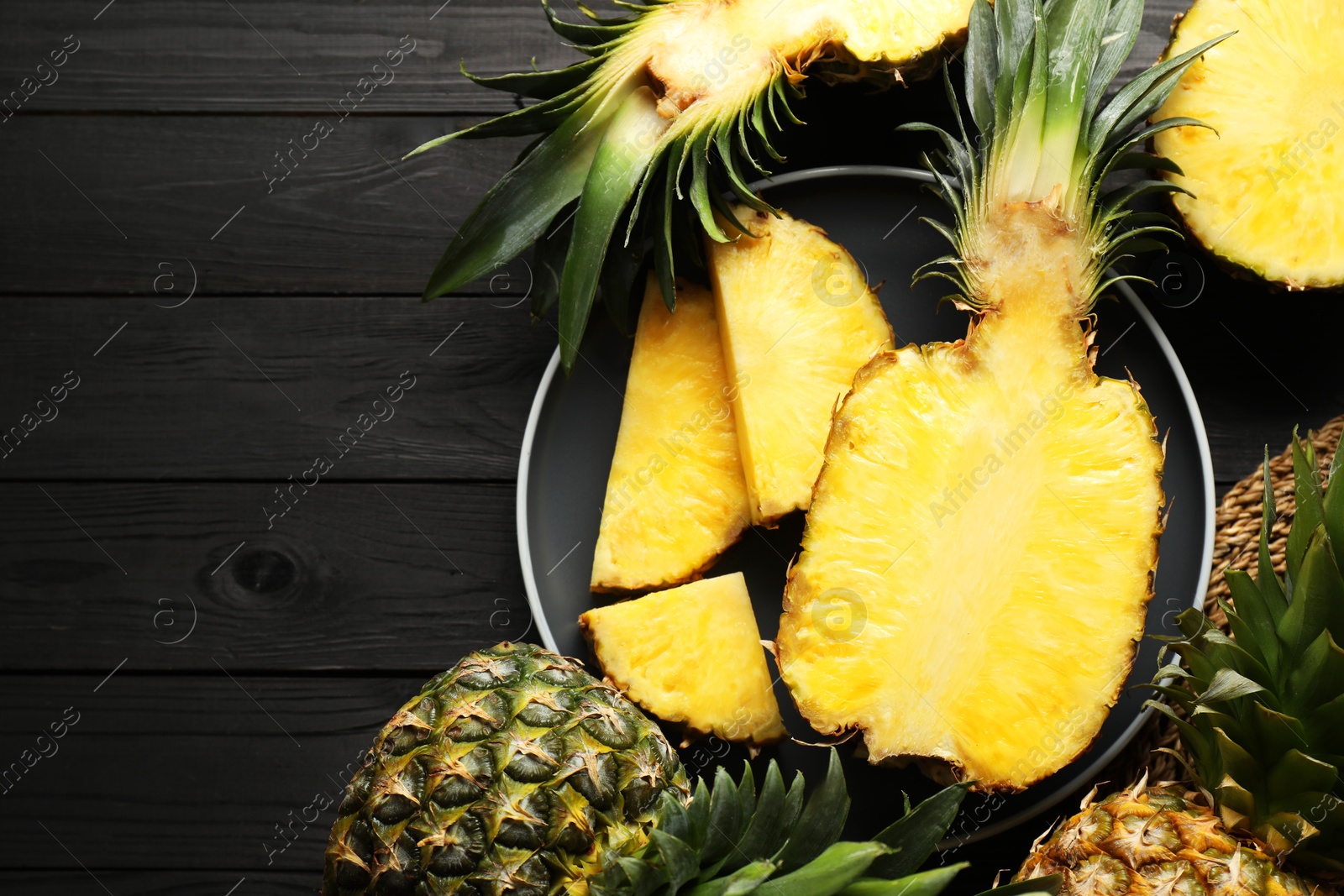 Photo of Fresh ripe pineapples on black wooden table, top view. Space for text