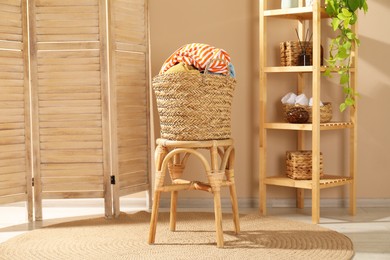 Photo of Wicker basket full of laundry on chair in bathroom