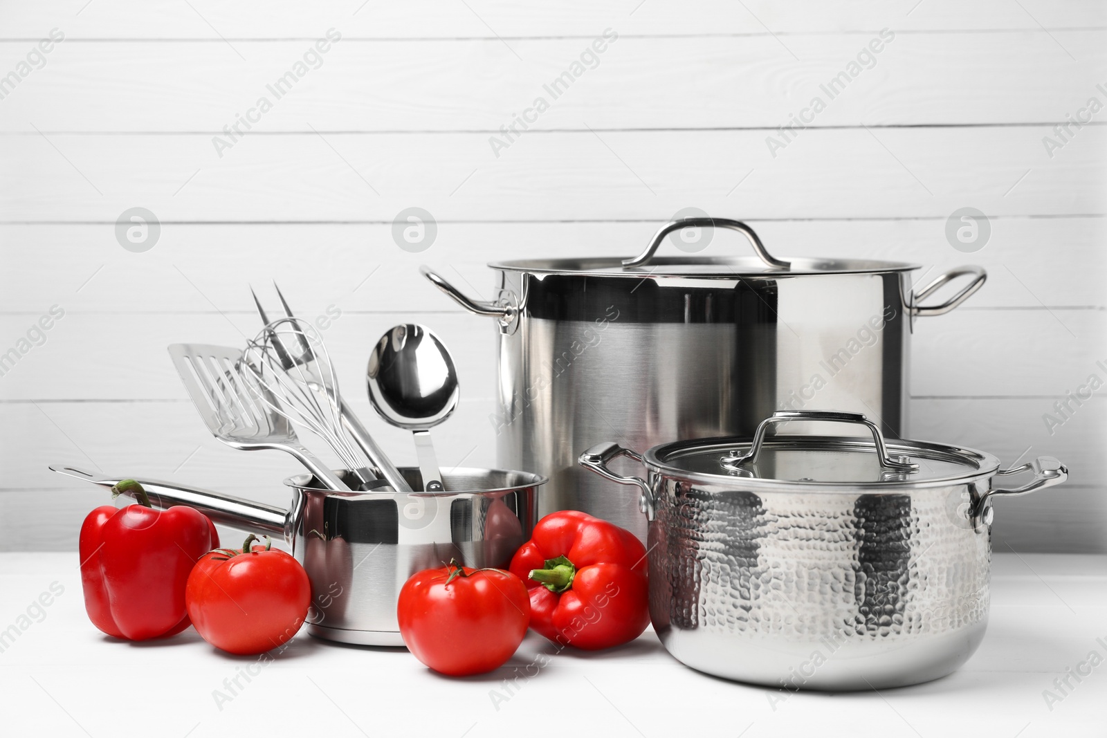 Photo of Dishware and cooking utensils with vegetables on white table