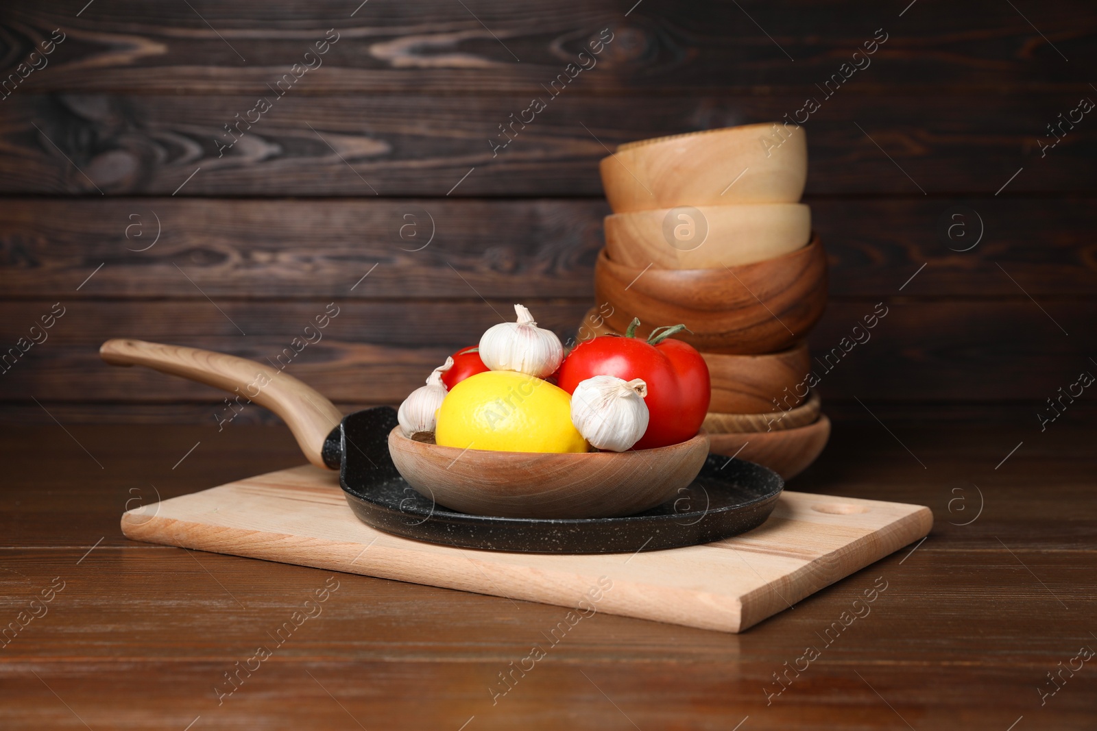 Photo of Bowls, frying pan with vegetables and lemon on wooden table. Cooking utensils