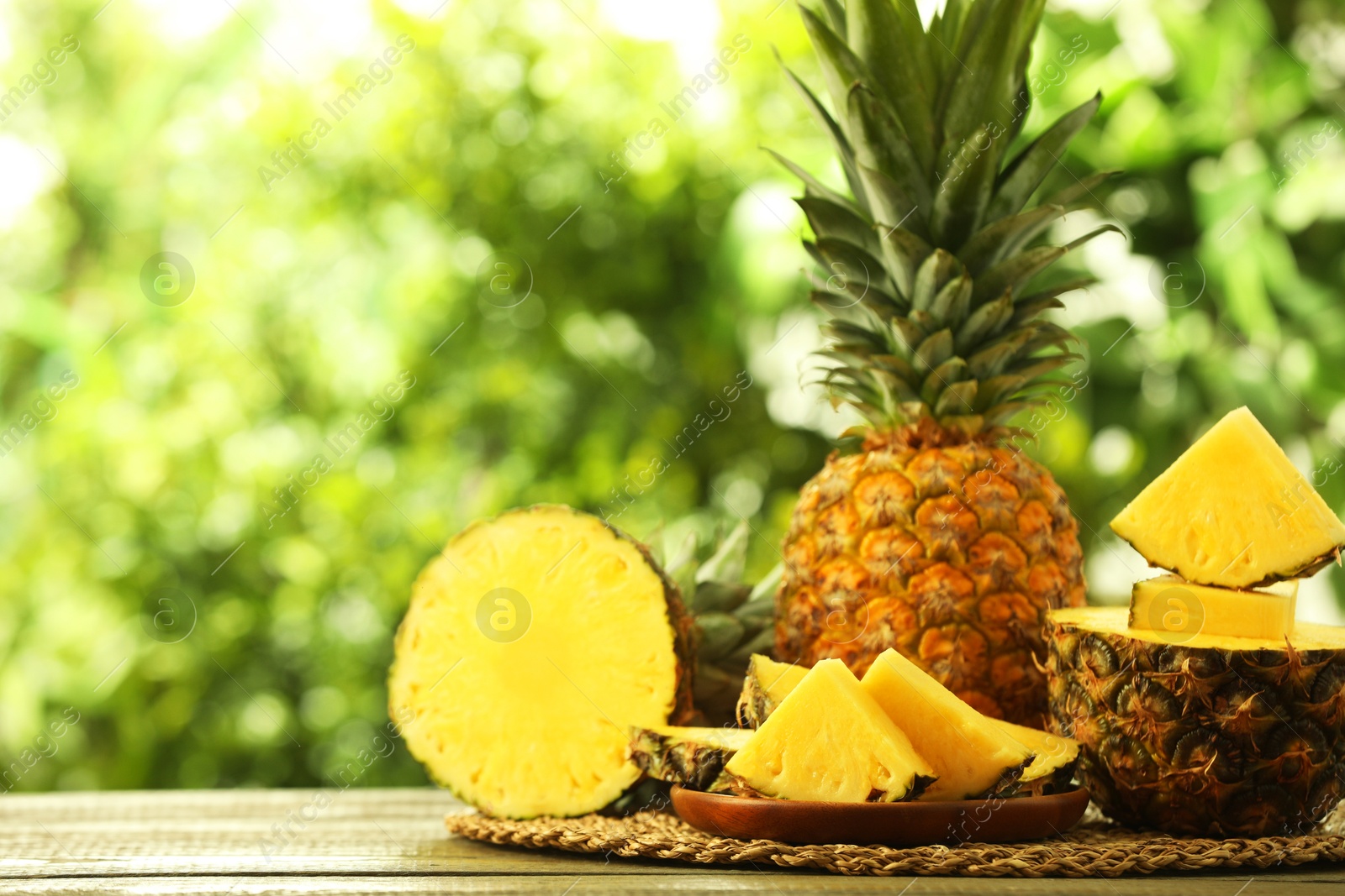 Photo of Fresh ripe pineapples on wooden table against blurred background, space for text