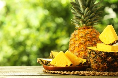 Photo of Fresh ripe pineapples on wooden table against blurred background, space for text