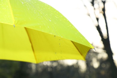 Photo of Open yellow umbrella under pouring rain outdoors, closeup