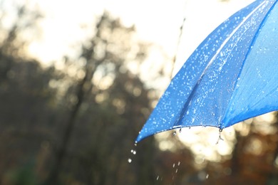 Photo of Open blue umbrella under pouring rain outdoors, closeup. Space for text