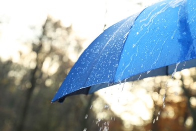 Photo of Open blue umbrella under pouring rain outdoors, closeup. Space for text