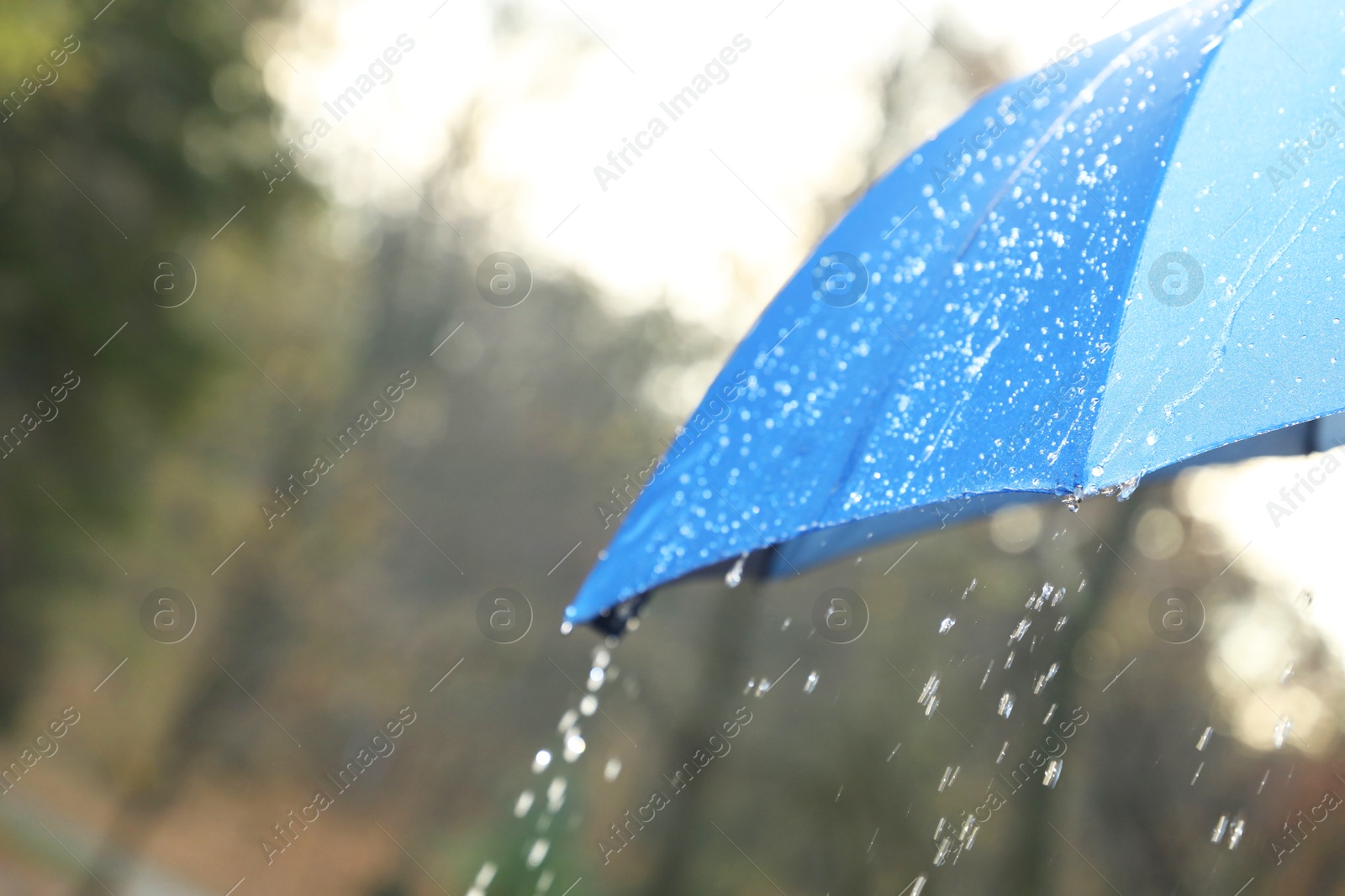 Photo of Open blue umbrella under pouring rain outdoors, closeup. Space for text