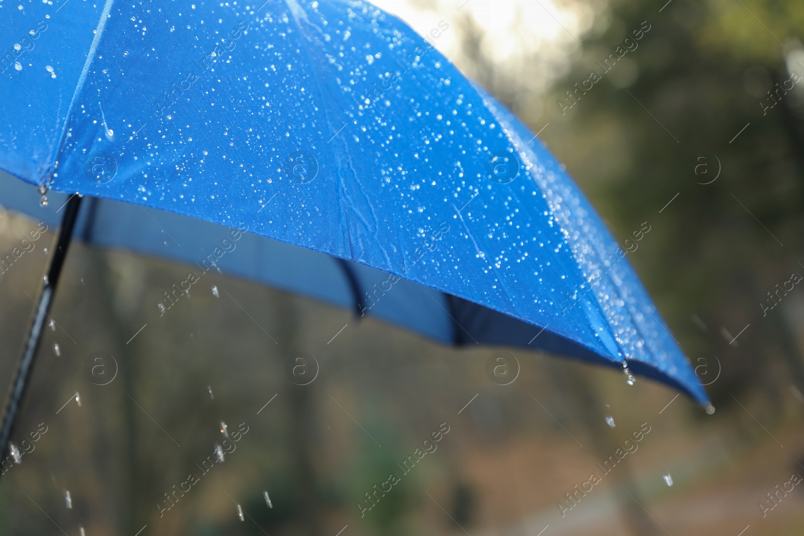 Photo of Open blue umbrella under pouring rain outdoors, closeup