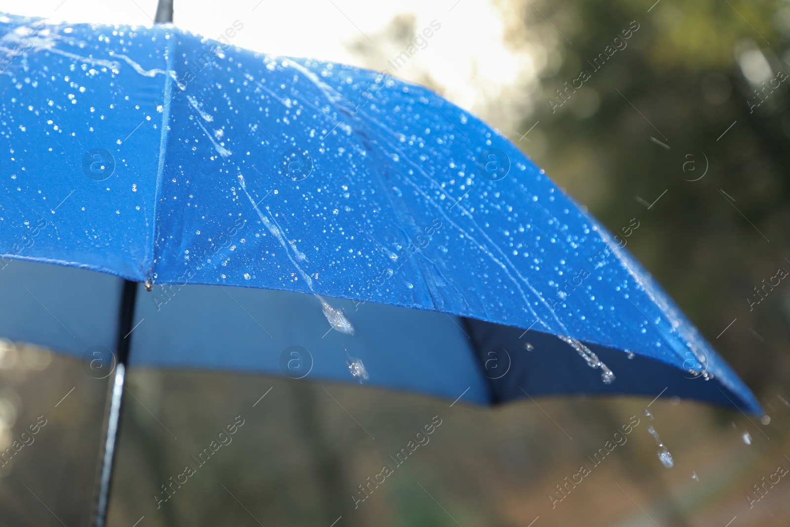 Photo of Open blue umbrella under pouring rain outdoors, closeup