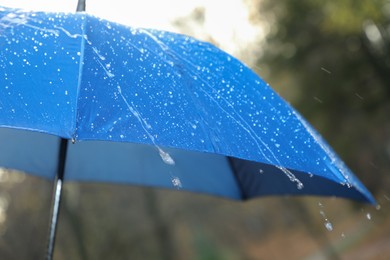 Photo of Open blue umbrella under pouring rain outdoors, closeup