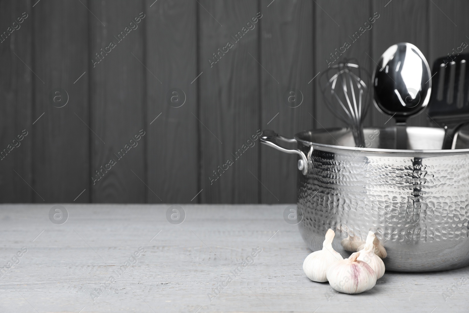 Photo of Dishware, cooking utensils and garlic on grey wooden table. Space for text