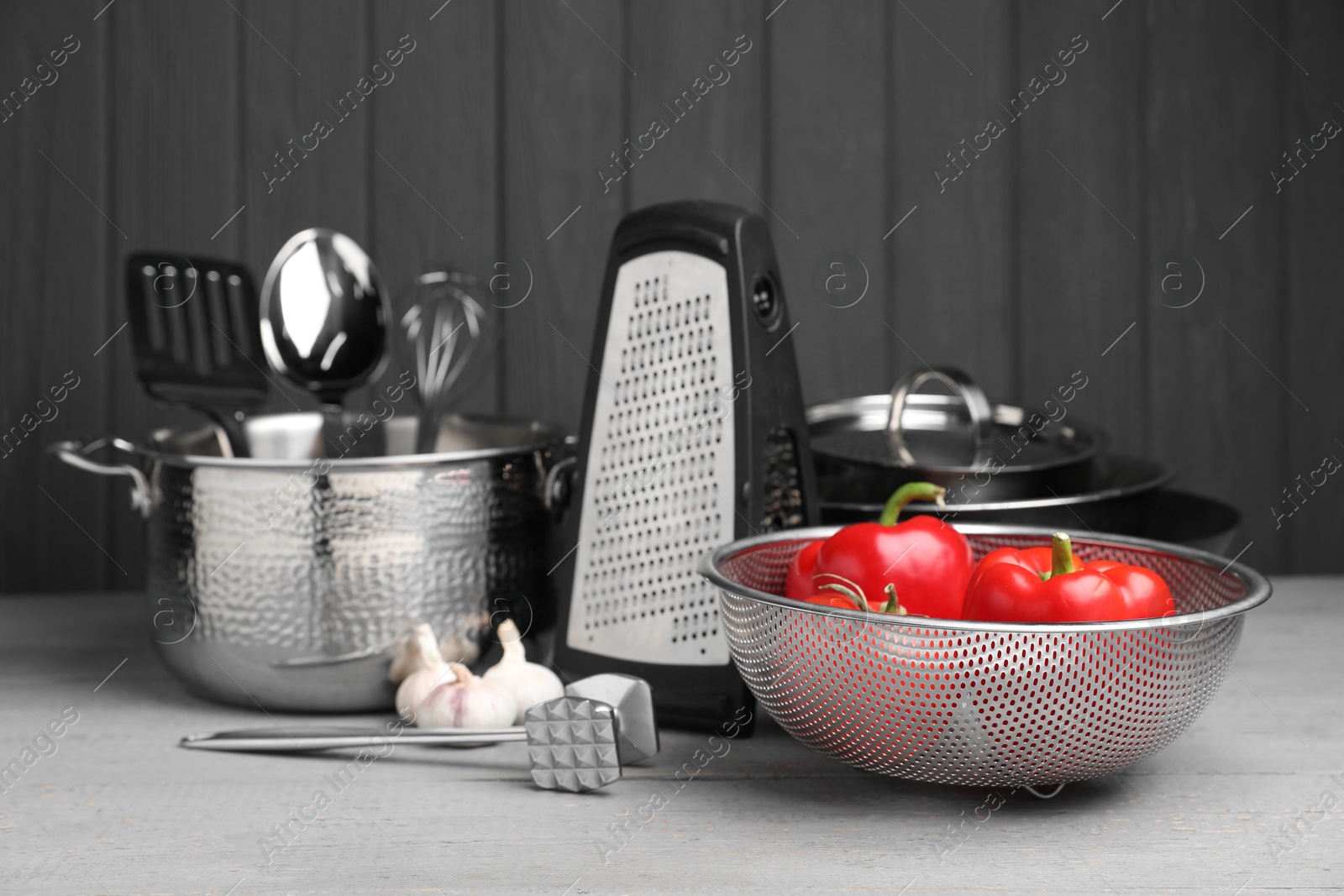 Photo of Dishware, cooking utensils, vegetables and garlic on grey wooden table