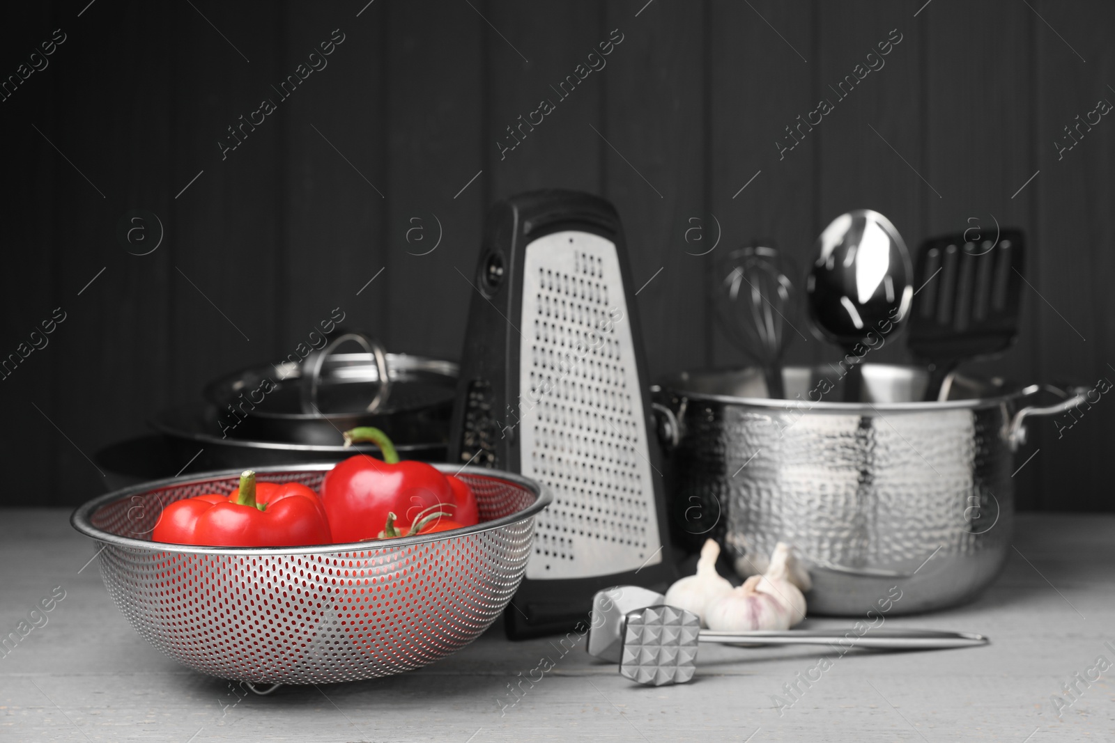 Photo of Dishware, cooking utensils, vegetables and garlic on grey wooden table